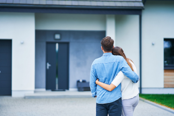 2 poeple holding eachother looking at a black front door of a house.