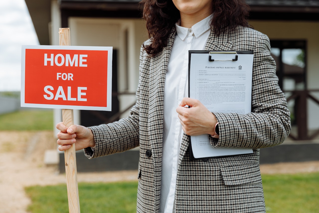 person holding a home for sale sign and a clipboard
