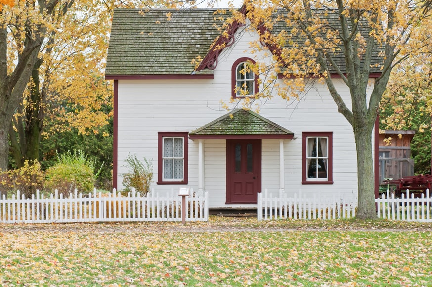 white house with red trim. Fall leaves on the ground and on the trees