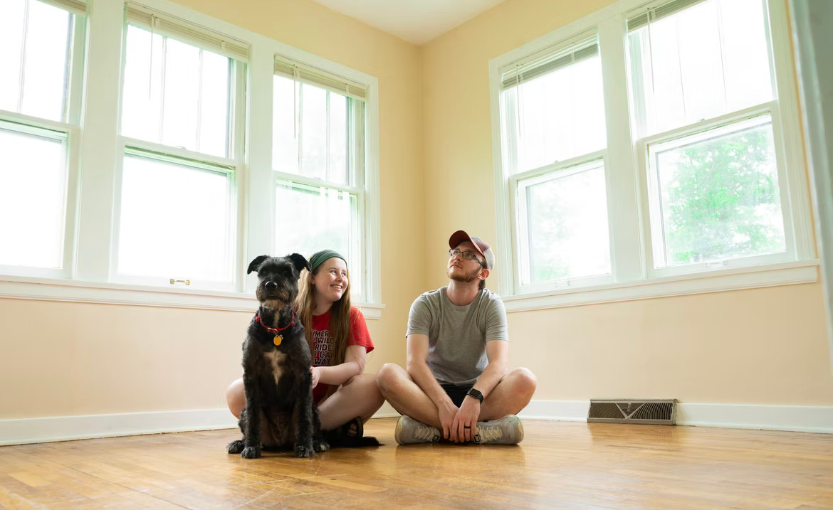 2 people and a dog sitting in the middle of the floor in an empty room