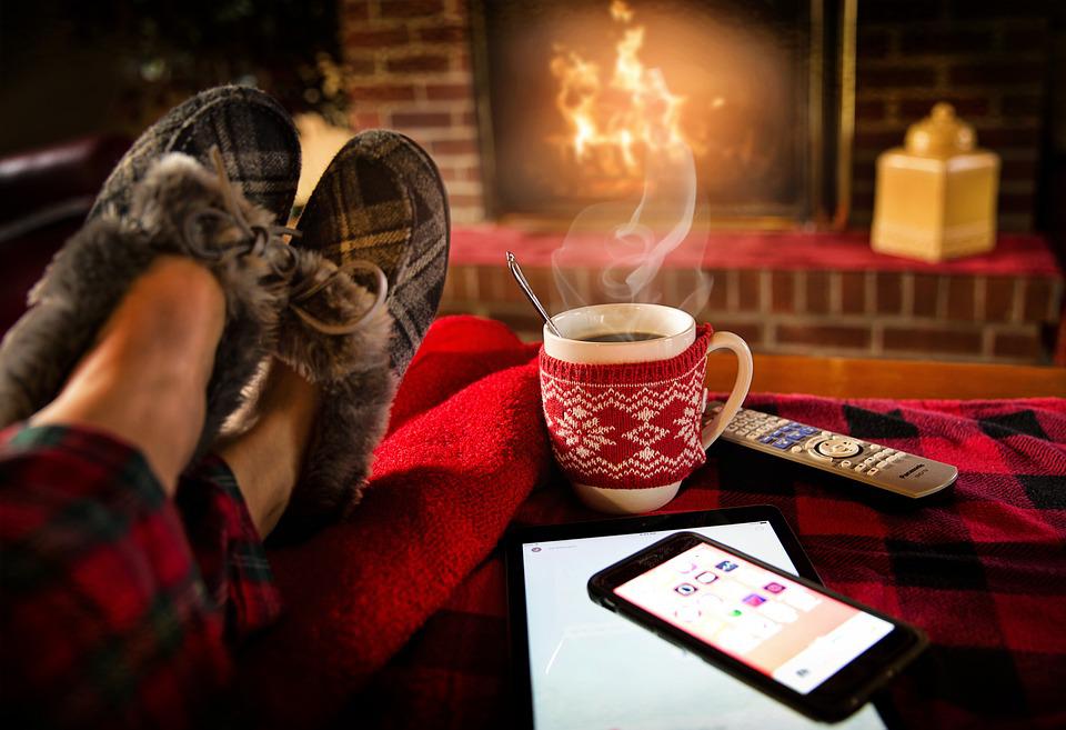 Feet up on a table, coffe steaming in a mug, phone, tablet and remote on the table