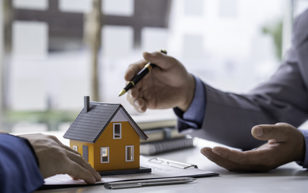 Tiny yellow house on a table. Hands from two people