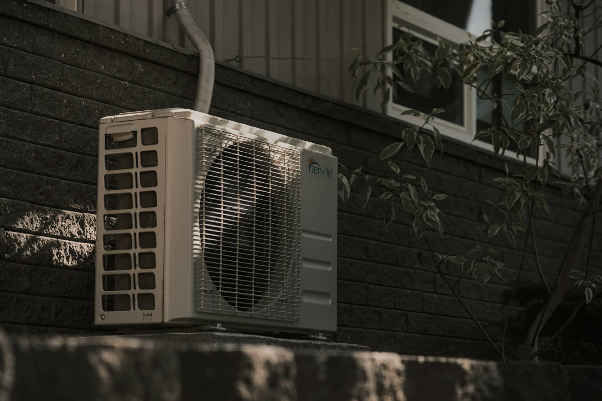 Air conditioning unit next to a brick wall. Image by Unsplsh