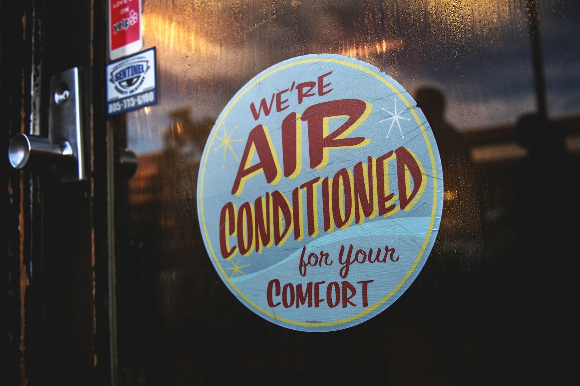 Sign on a door 'we're air conditioned for your comfort'. Image by Unsplash