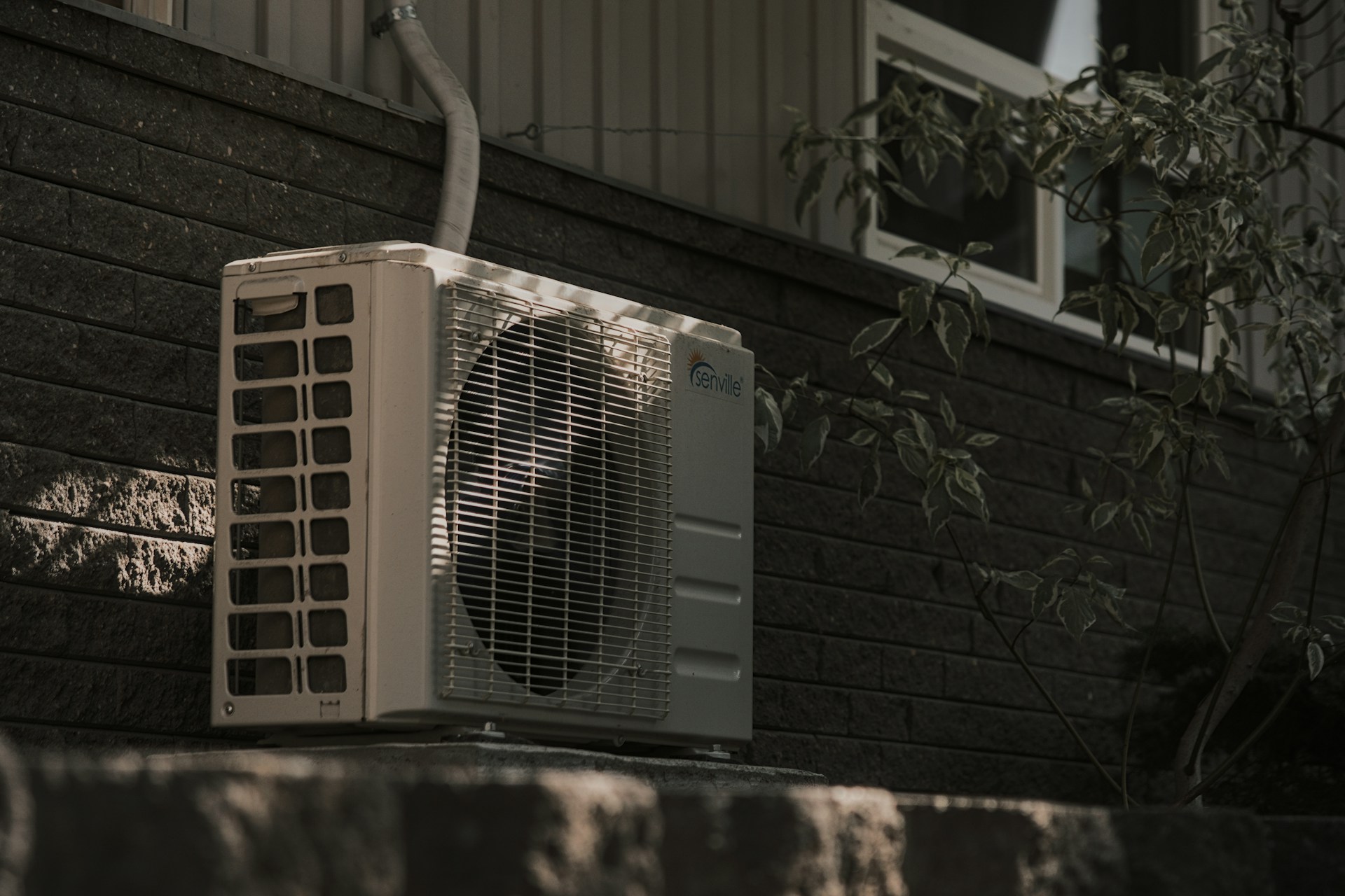 A white HVAC unit mounted on a brick wall. Image by Unsplash