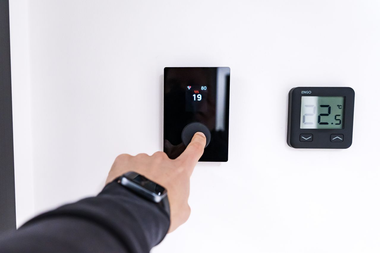 A person adjusting a thermostat on a wall. Image by Pexels