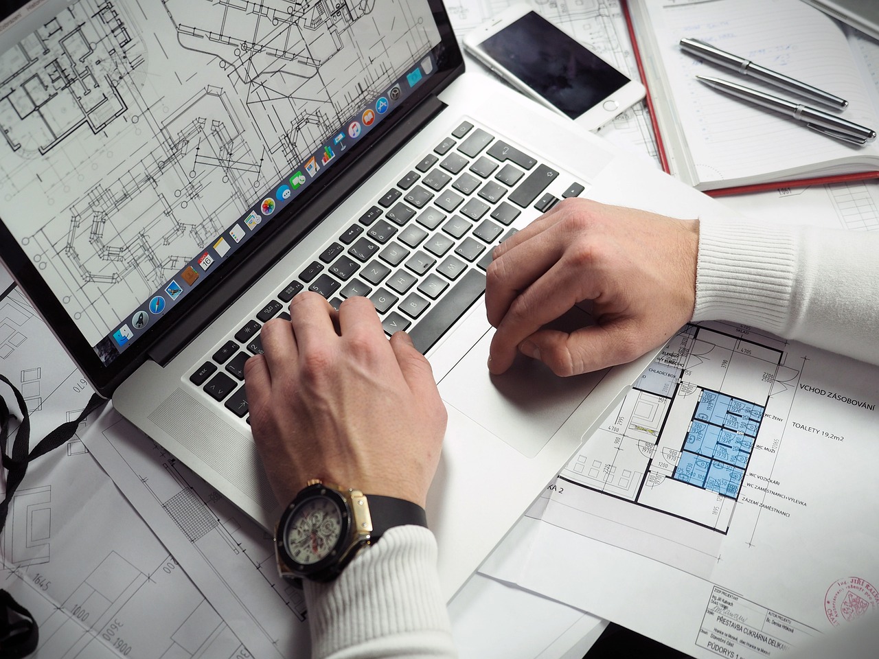 Person with a laptop reviewing blueprints during a site planning session. Image by Pixabay