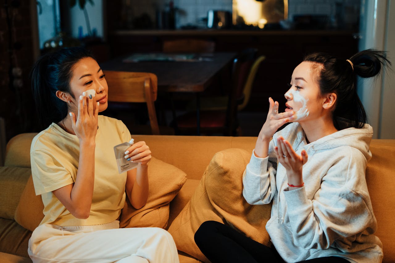 2 people sitting on a sofa putting on facial masks. Image by Pexels