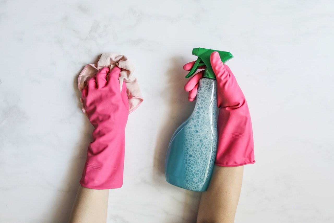 two hands with pink gloves, spray bottle in one hand and a rag in the other hand