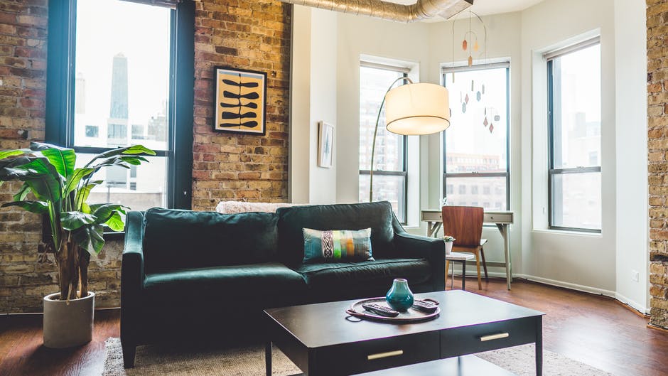 A green sofa inside an apartment with large windows. Image by Pexels