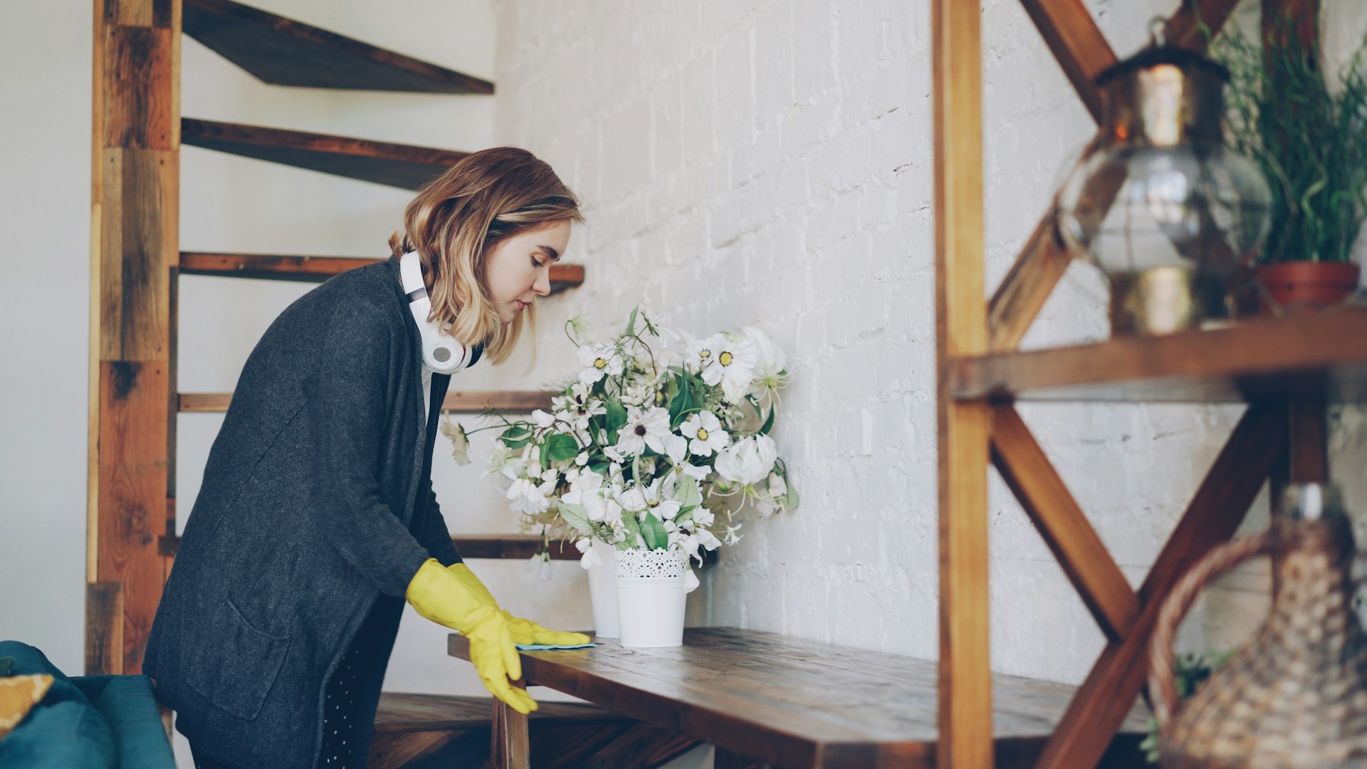 Woman in yellow gloves cleaning a shelf inside an apartment. Image via Unsplash
