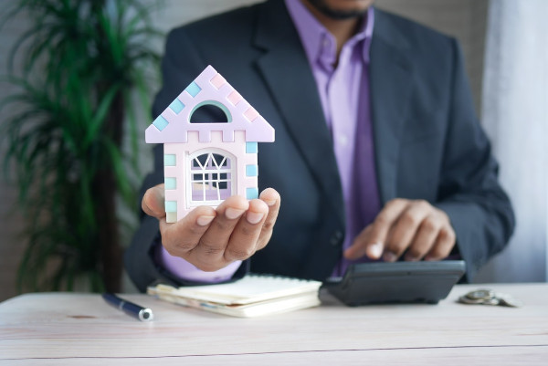 person in with a suit and purple tie, holding a house in his hand