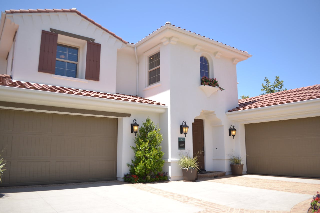 White concrete house with 2 brown garage doors. Image by Pexels