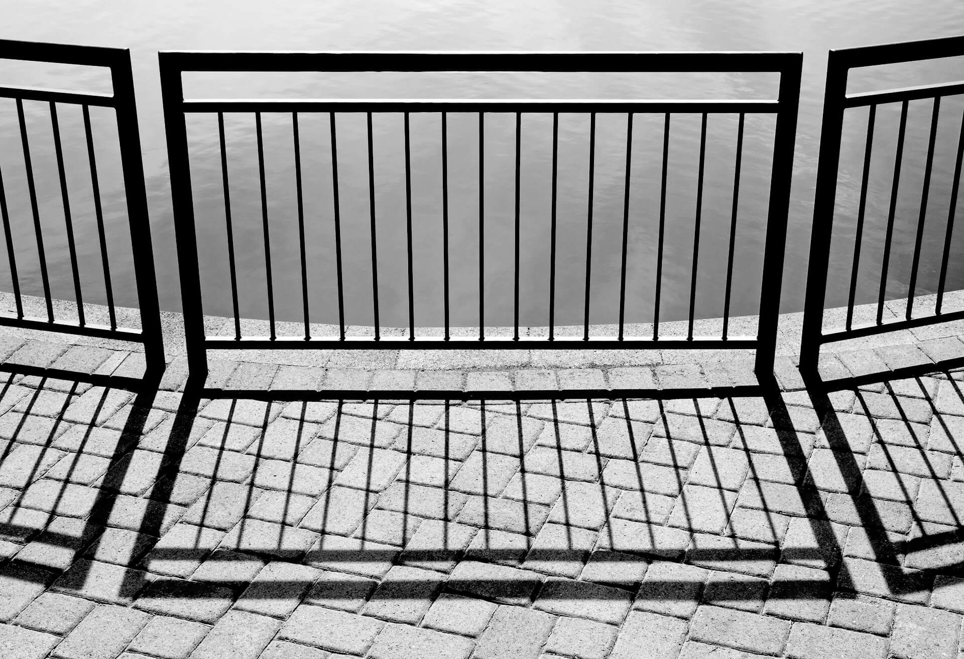 black metal railing casts shadows on paved ground. Image by Unsplash