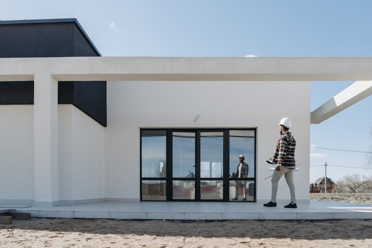 Contractor walking in front of a white concrete house. Image by Pexels