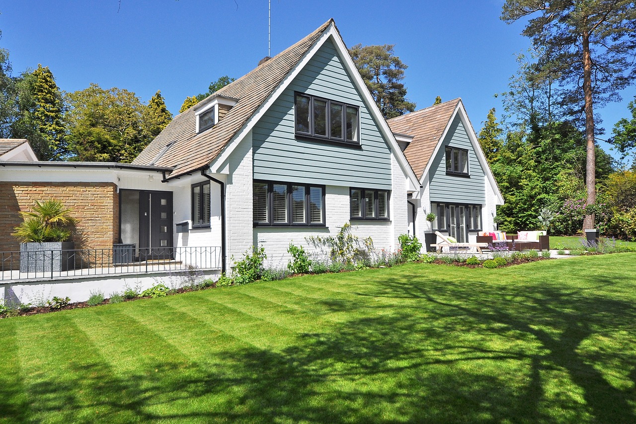 White and blue house, large green lawn, houses behind the house. Image by Pixabay