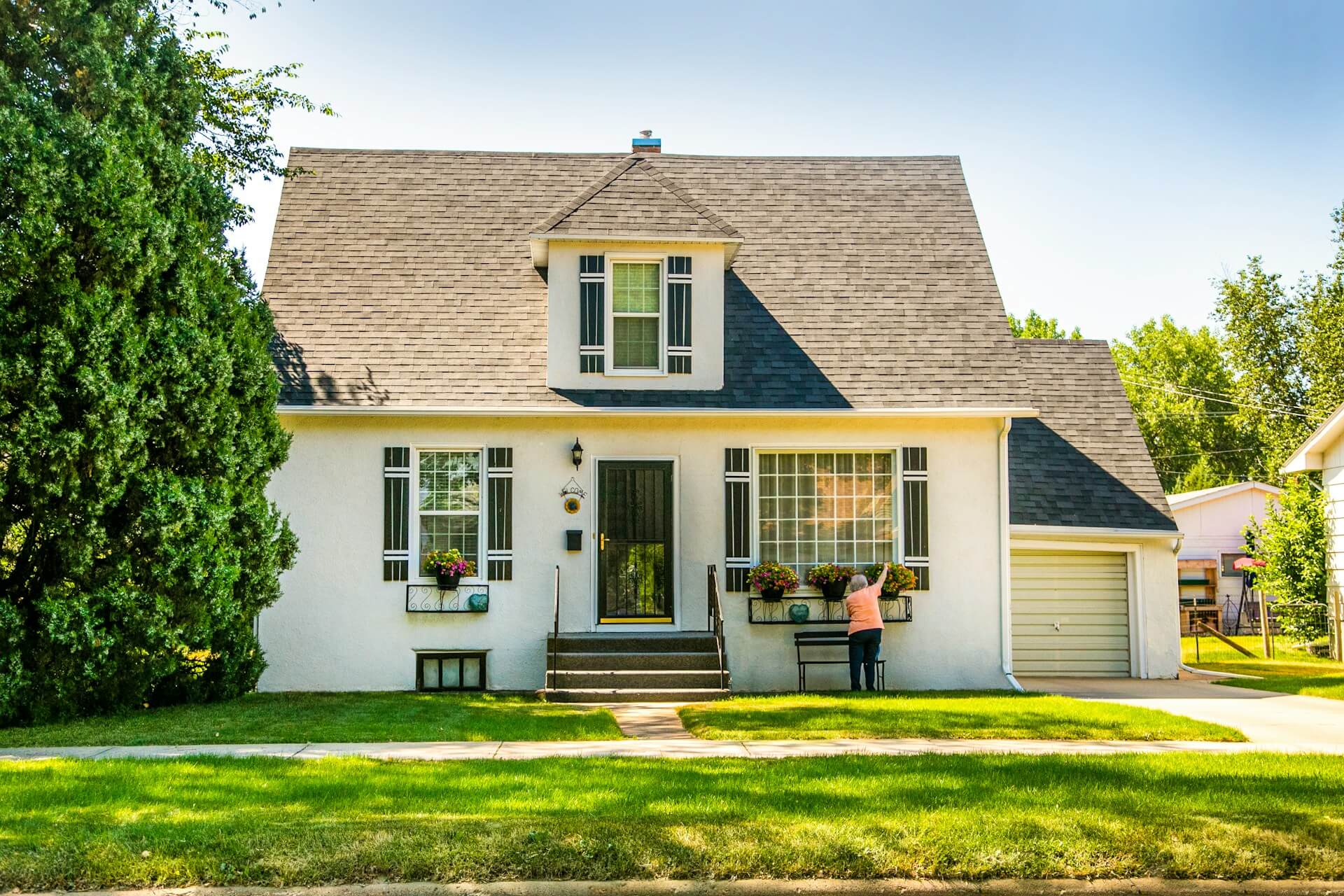 White house with green lawn and mature trees representing thoughtful outdoor property improvements. Image via Unsplash