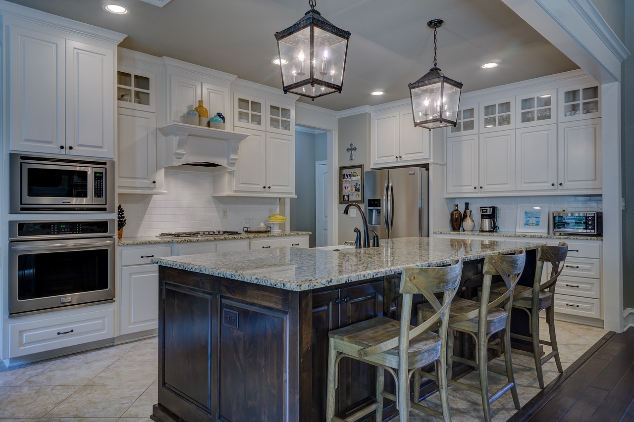 White kitchen cabinets, brown, wooden island with 3 chairs. Image by Pixabay