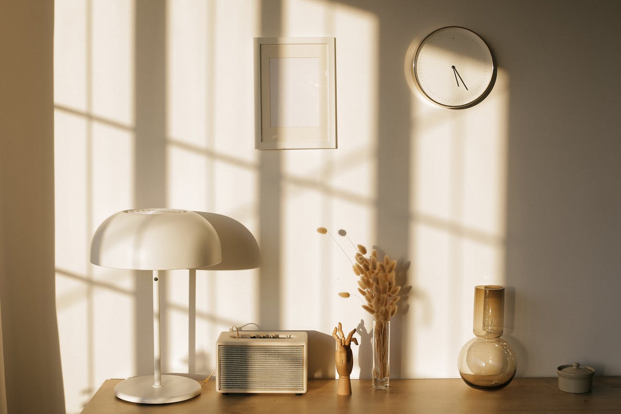 Lamp, vase, radio, on a table near a wall with a clock and a frame. Image by Pexels