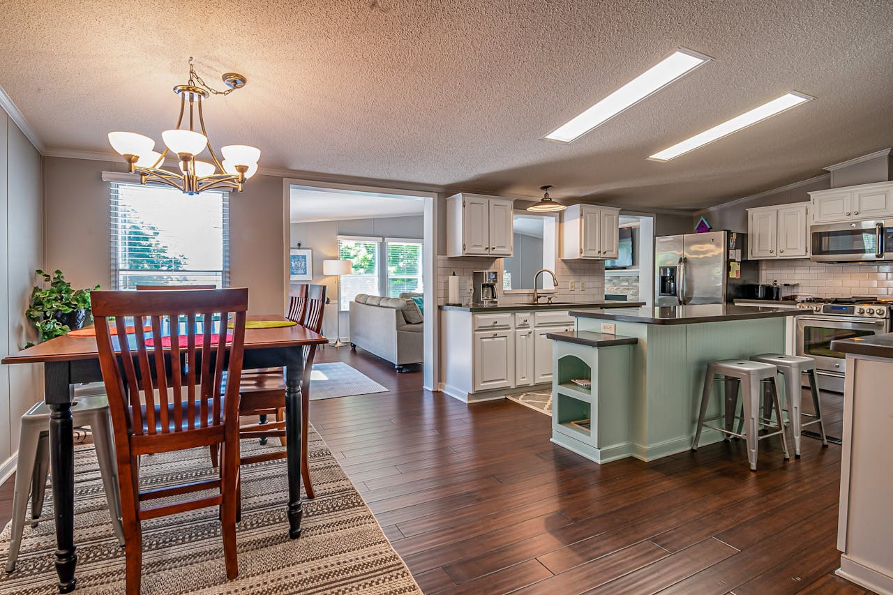 Large eat-in kitchen, white cabinets, green kitchen island. Rug under a table and chairs. Image by Pexels.