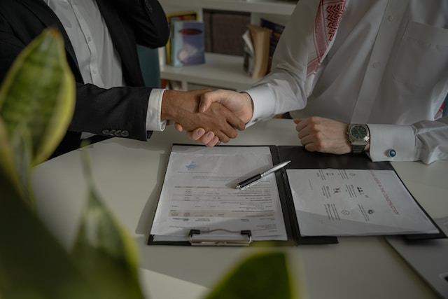 2 people shaking hands, paperwork and a pen on a table