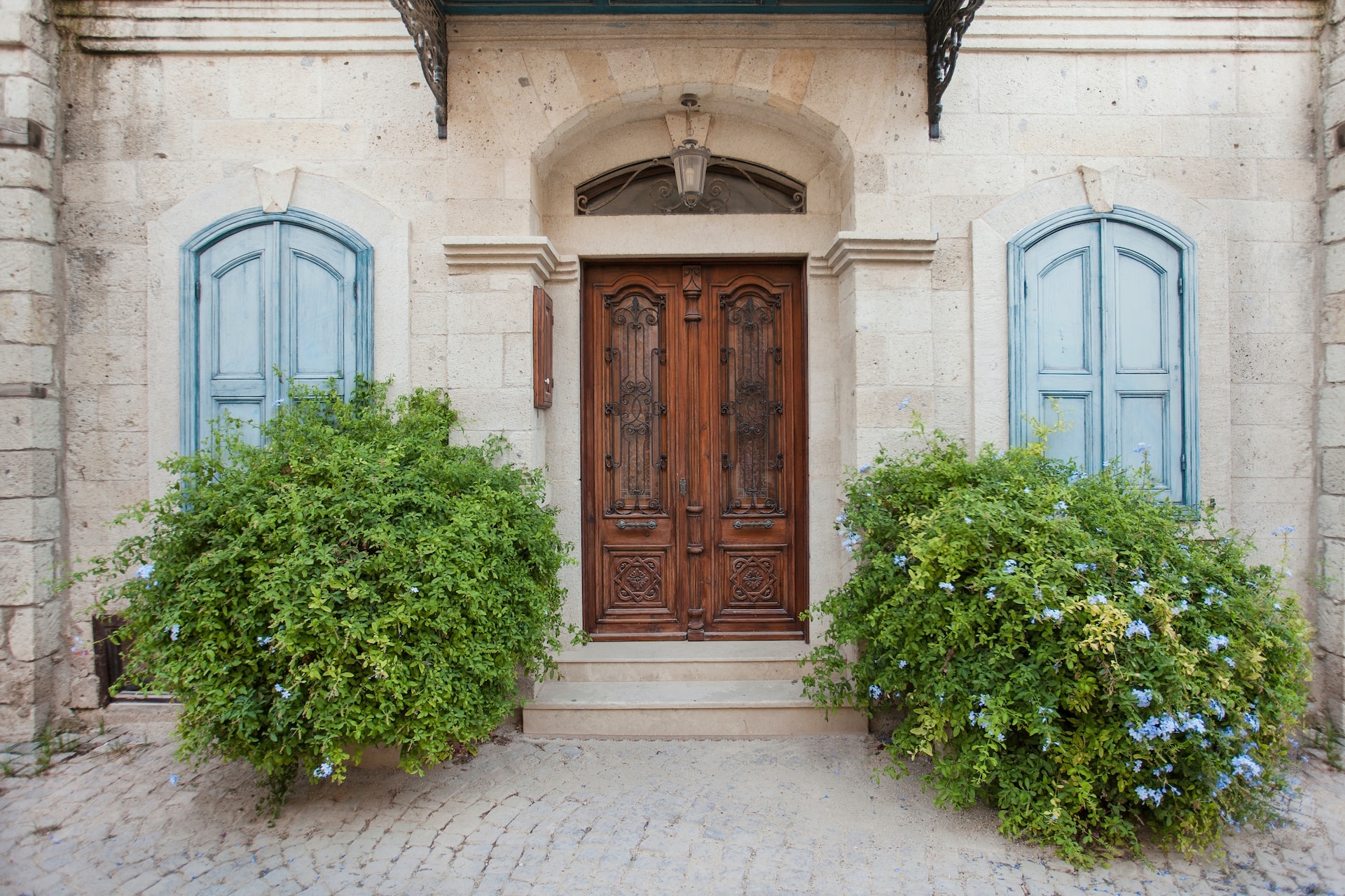 brown carved door, blu shutters, white house. Image from Unsplash