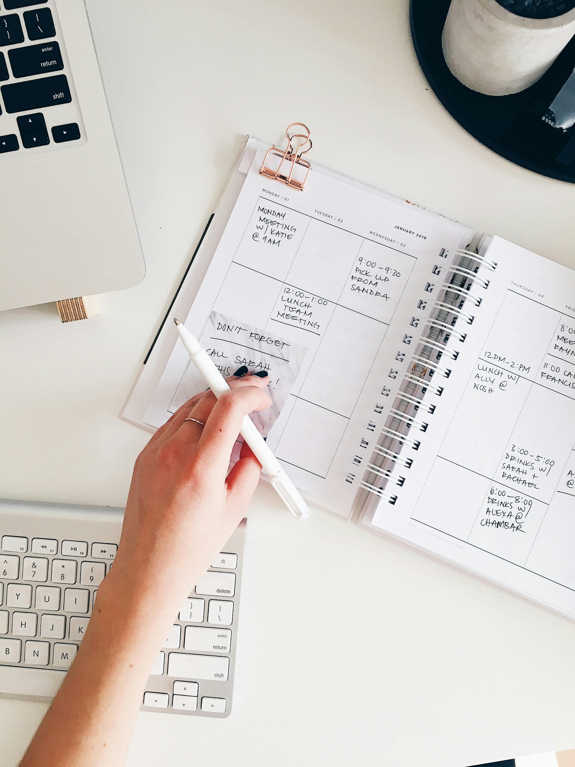 Person holding notepad and pen in flat lay photography arrangement for budget planning and rent expense tracking. Image via Unsplash