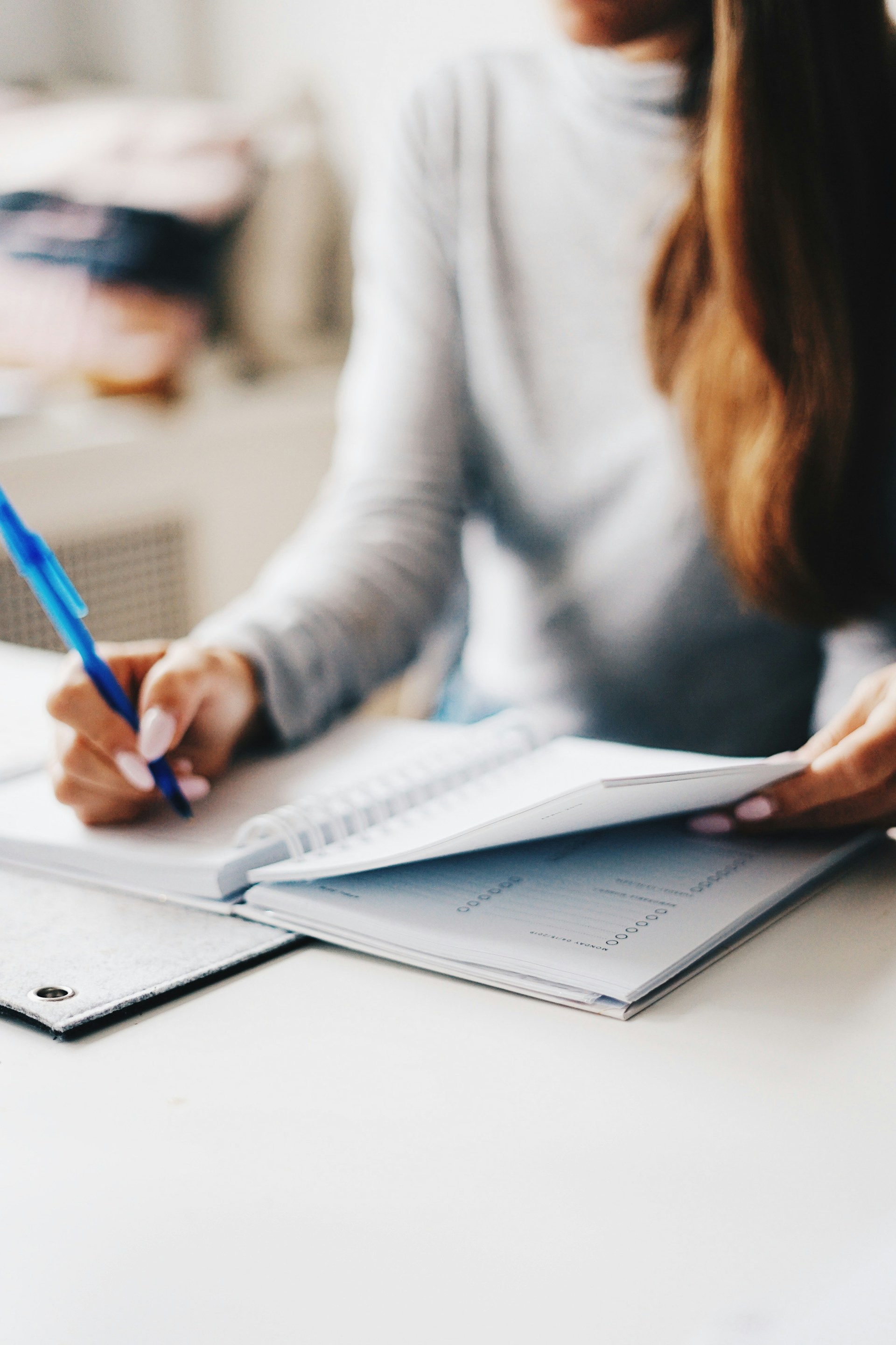 Woman writing in notebook with pen tracking monthly budget and savings goals for housing expenses. Image via Unsplash