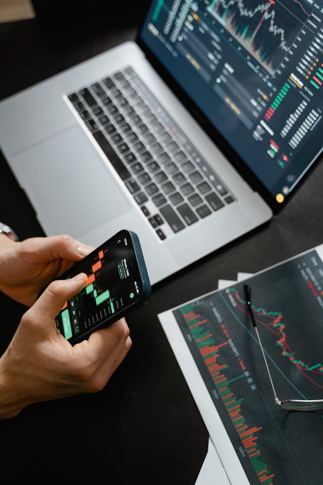 Person holding a phone, laptop and tablet on a table. Image by Pexels