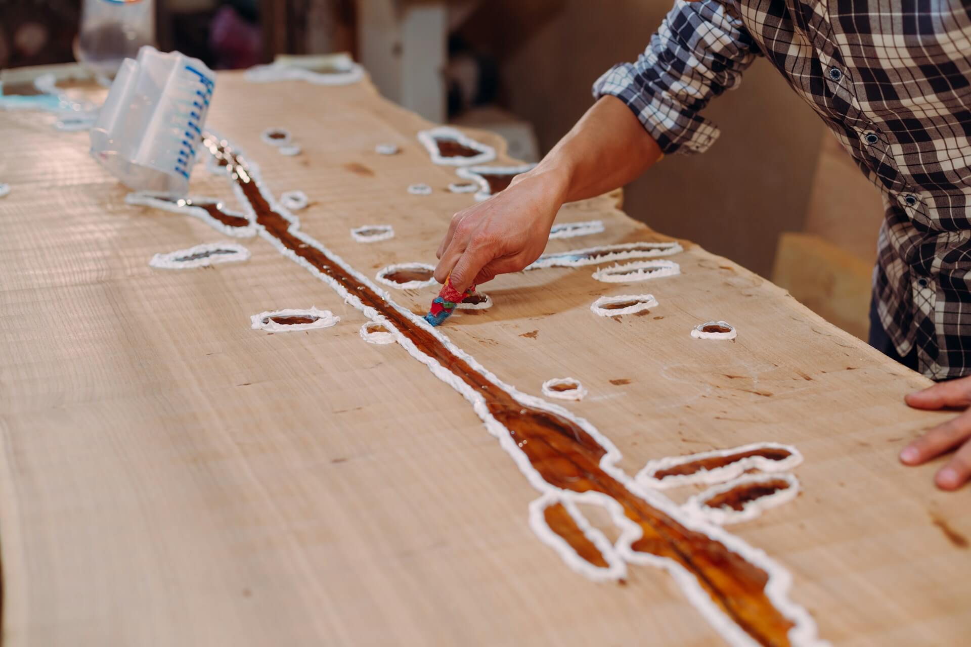 Carpenter cleaning the wooden table from epoxy resin drops in a workshop. Process of making a craft resin and wood table. Image by Unsplash