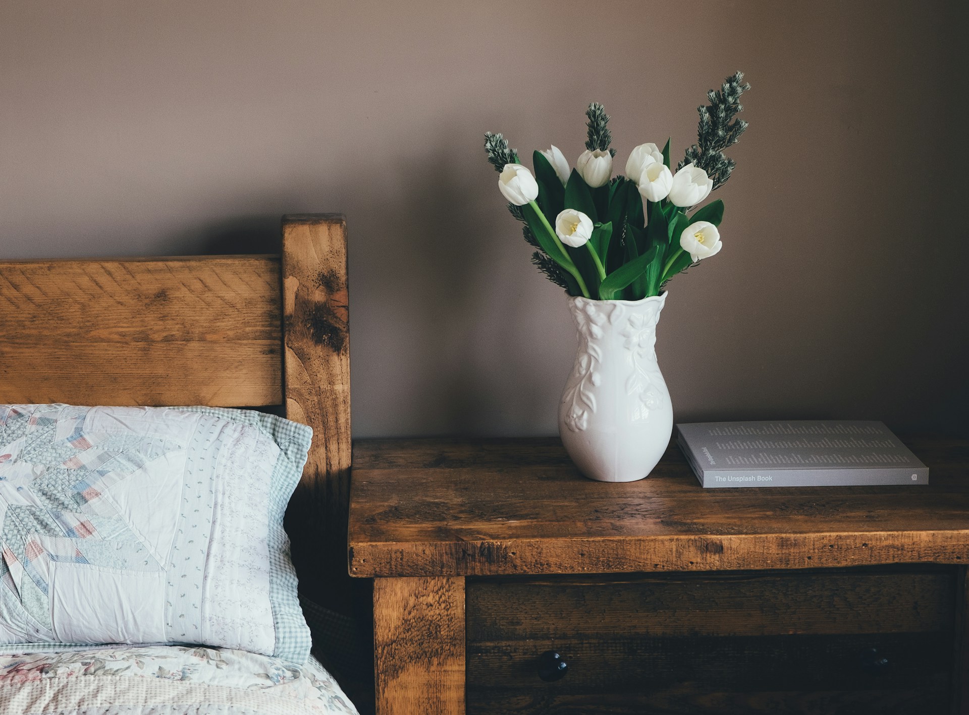 White flower vase on a nighttable next to a bed. Image by Unsplash