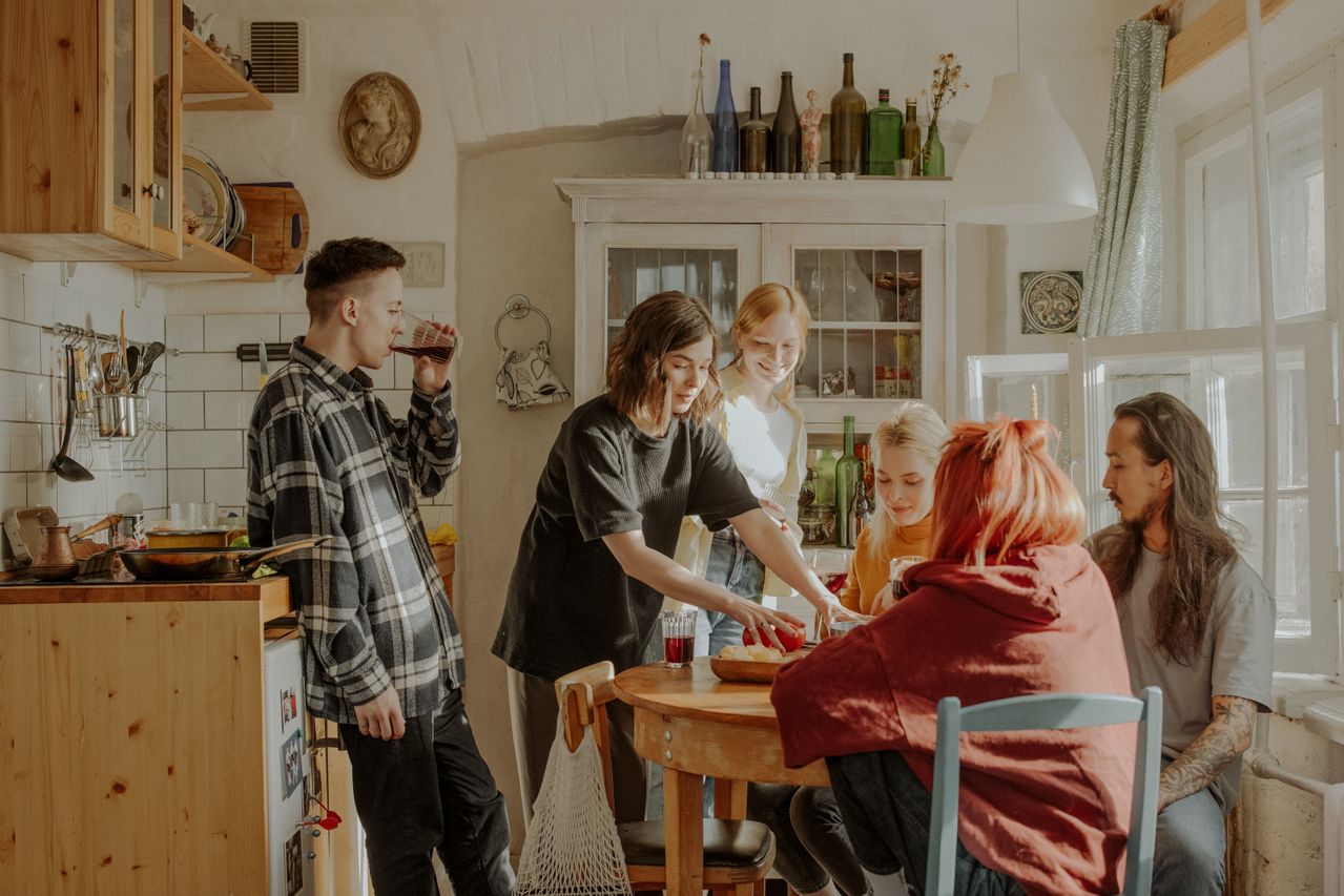 Friends gathered around a wooden dining table sharing a meal in a small apartment. Photo by cottonbro studio on Pexels