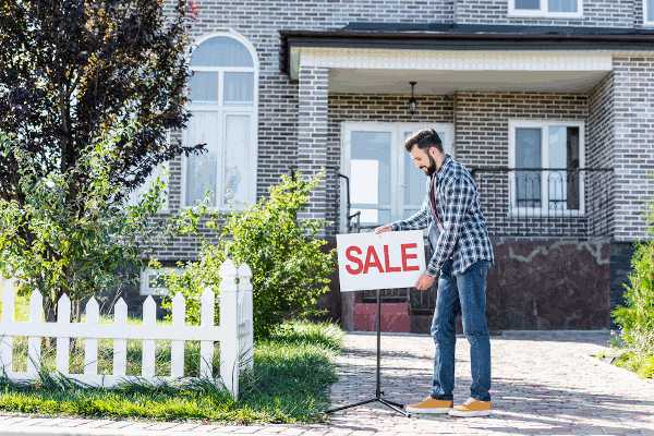person putting a for sale sign in front of a house