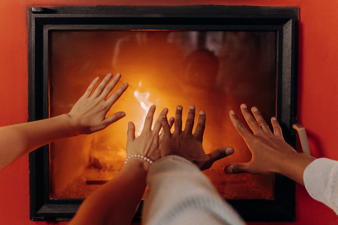 People heating their hands in front of a fireplace. Image by Pexels