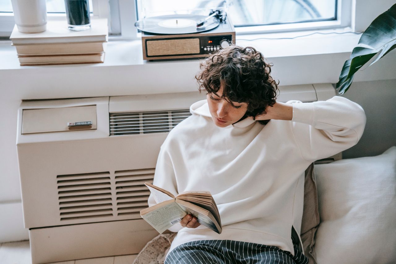 Person in a white hoodie reading peacefully at home, enjoying leisure time. Image by Pexels