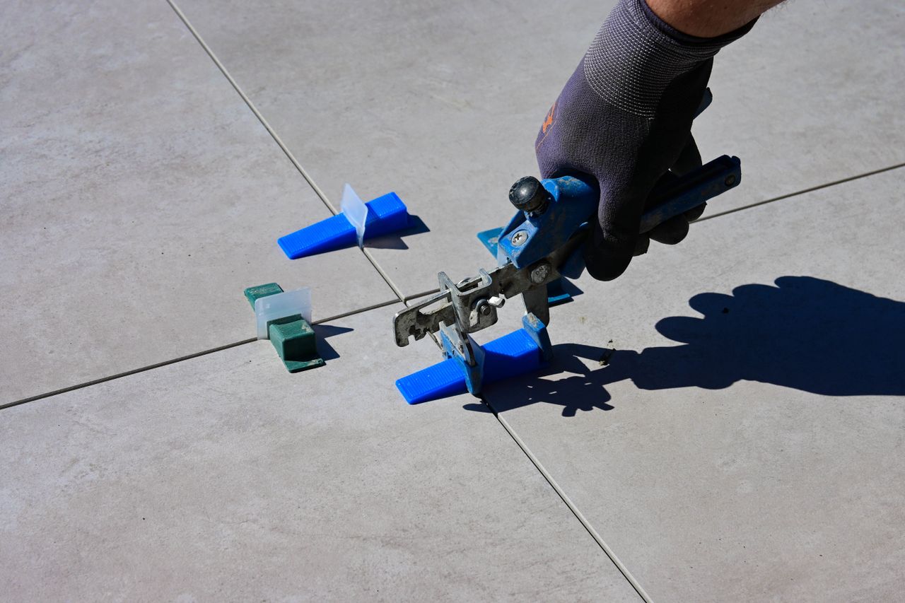 A gloved hand using a leveling tool to install tiles with spacers. Image by Pexels