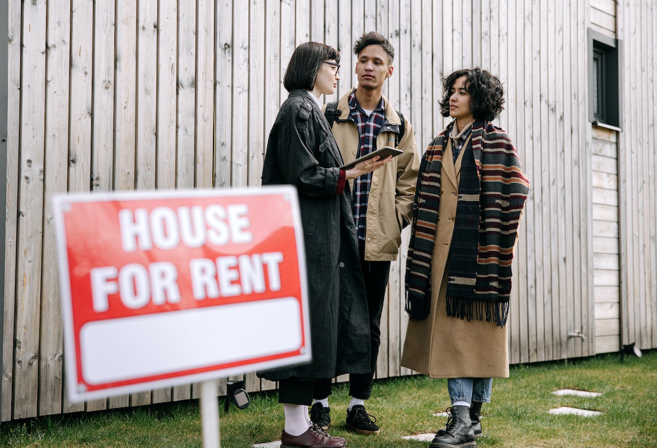 3 people in front of a for rent sign