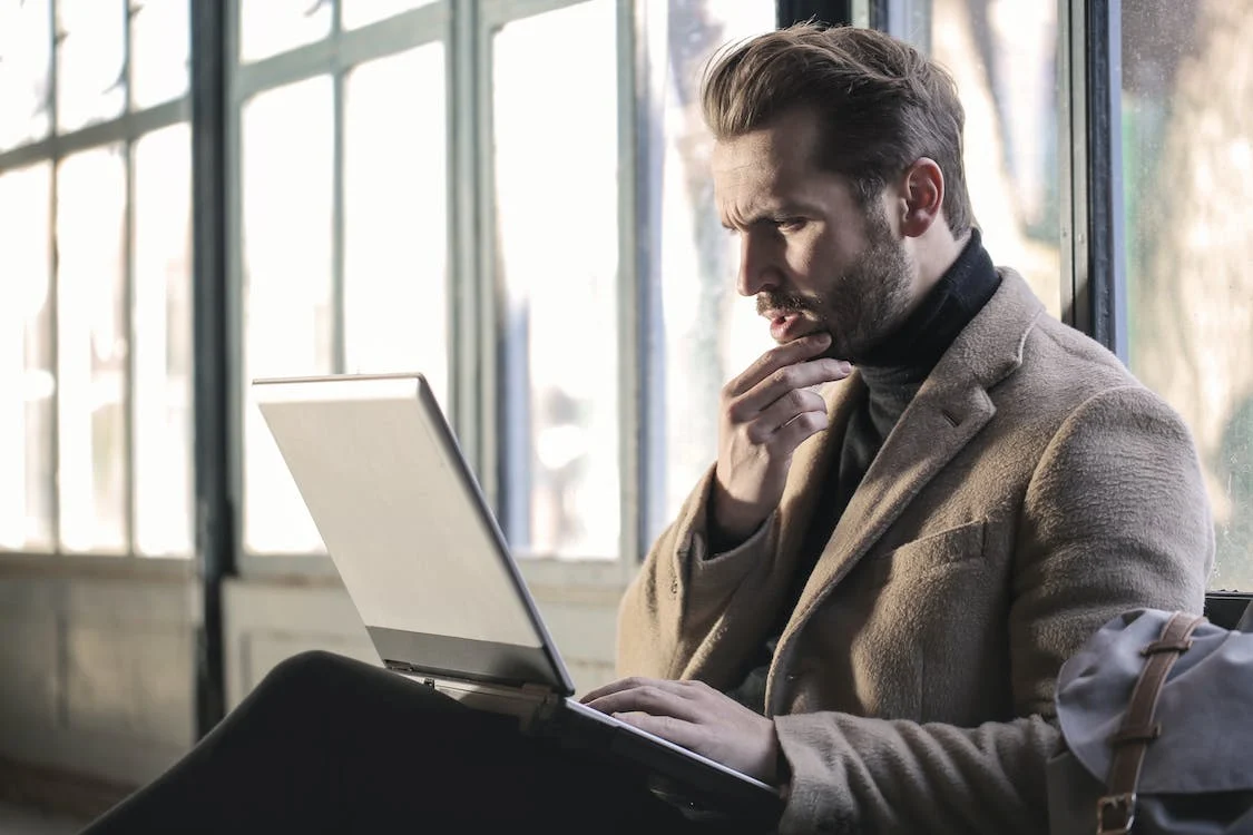 Man in a gray jacket sitting and looking at a laptop