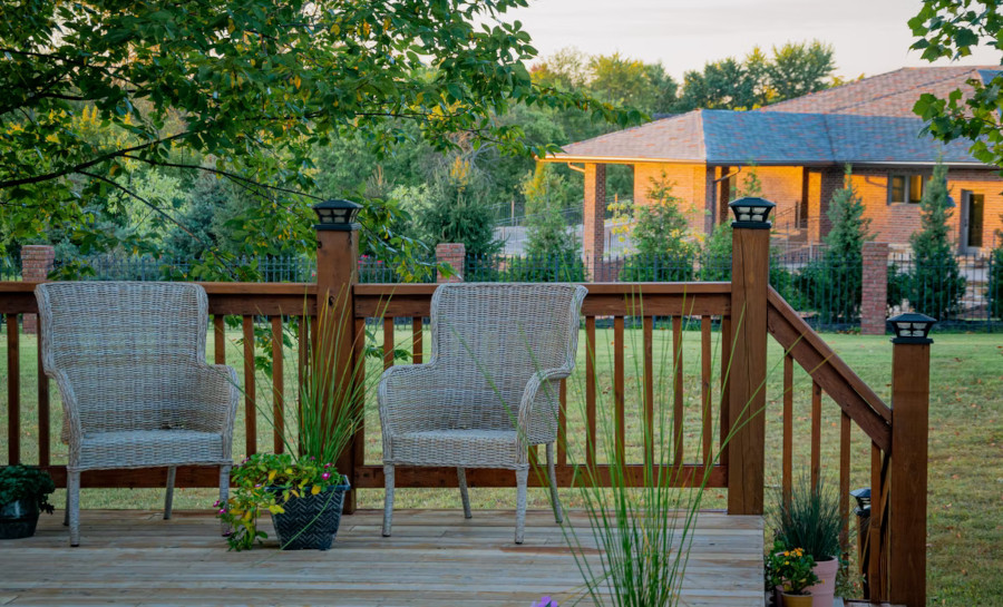 Backyard porch with a couple of chairs and flowers, lights on the fence