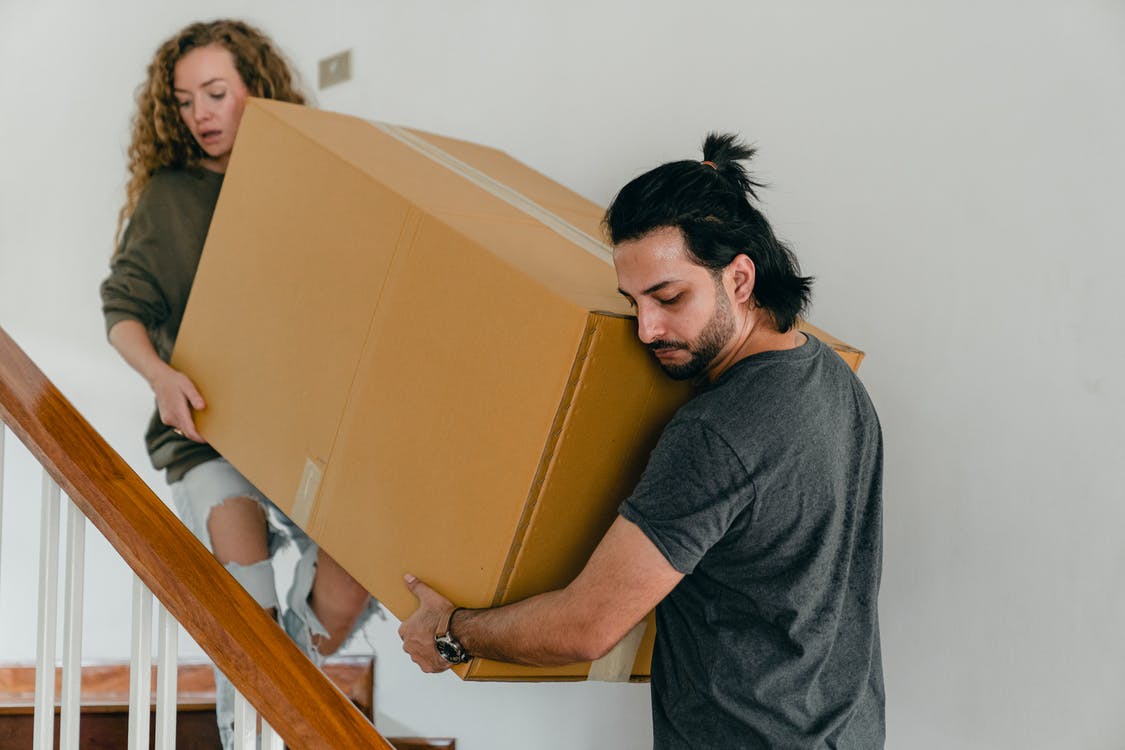 2 people carrying a large box up the stairs