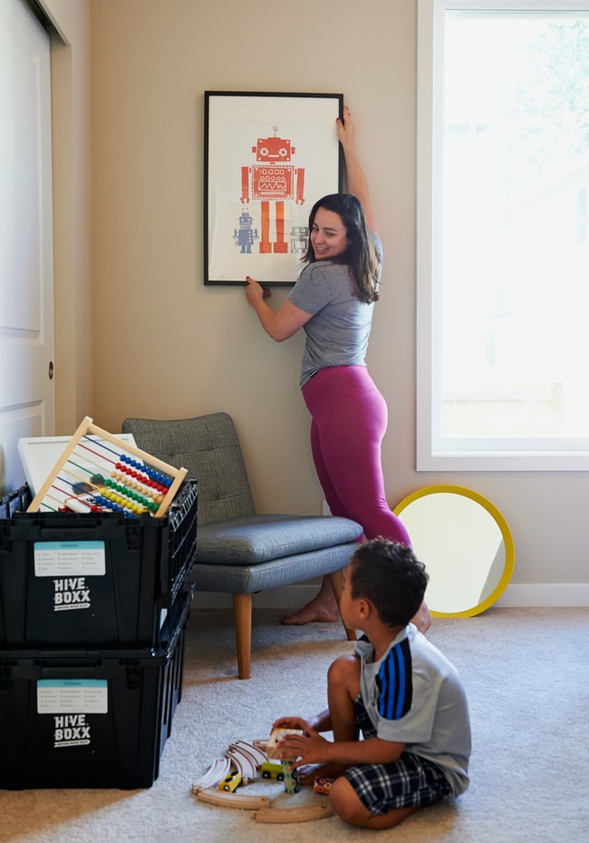 A person hanging or adjusting a painting. child sitting on floor.