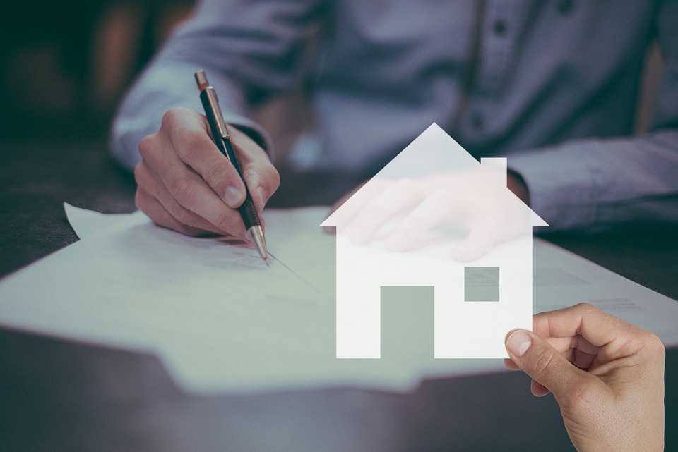 Person with a pen and paper, another person holding up a house made out of paper