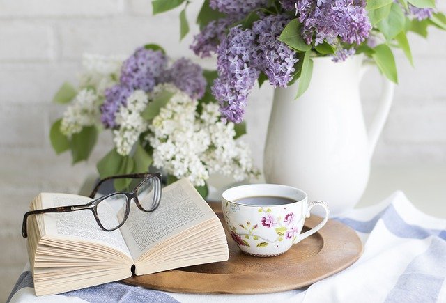 open book with glasses on top. cup of coffe, flowers in a pot