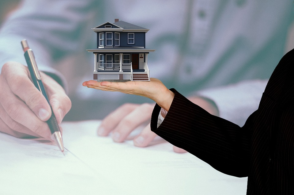 Person holding a house in their hand, person writing with a pen