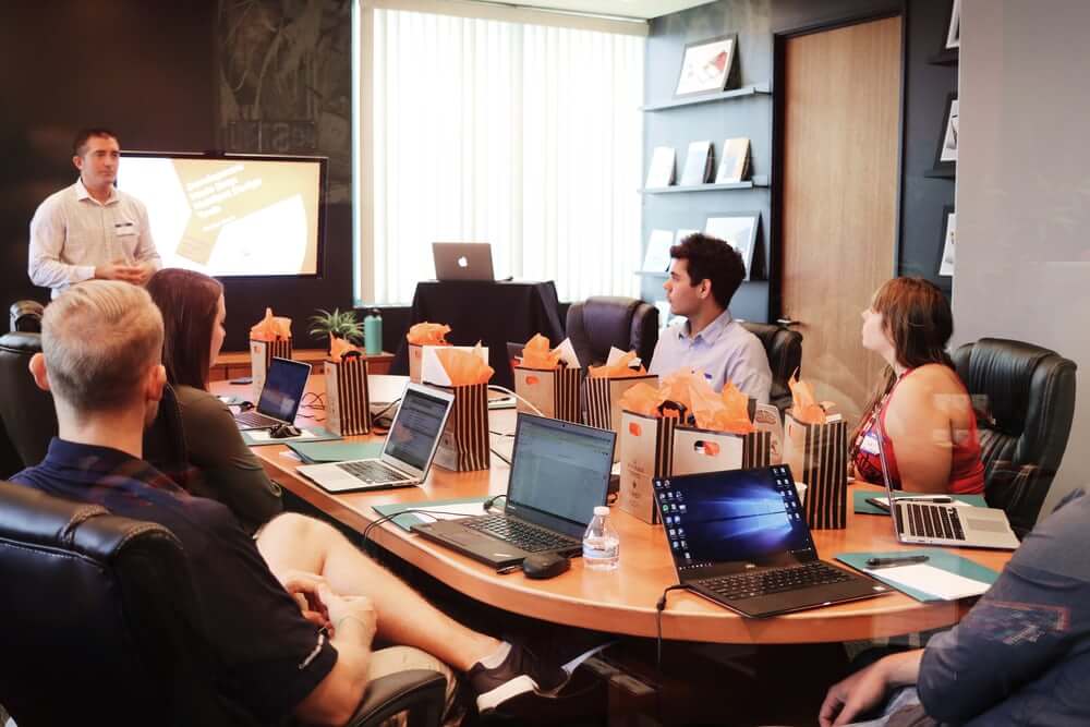 Business meeting, people sitting with laptops around a table.