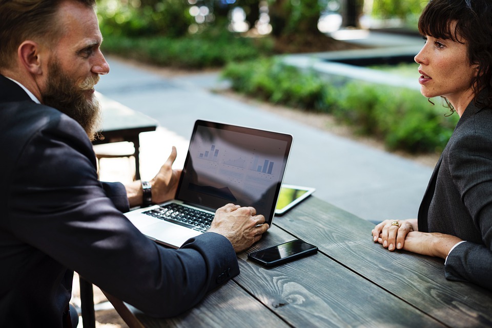 2 people sitting at a table with a computer and cellphone