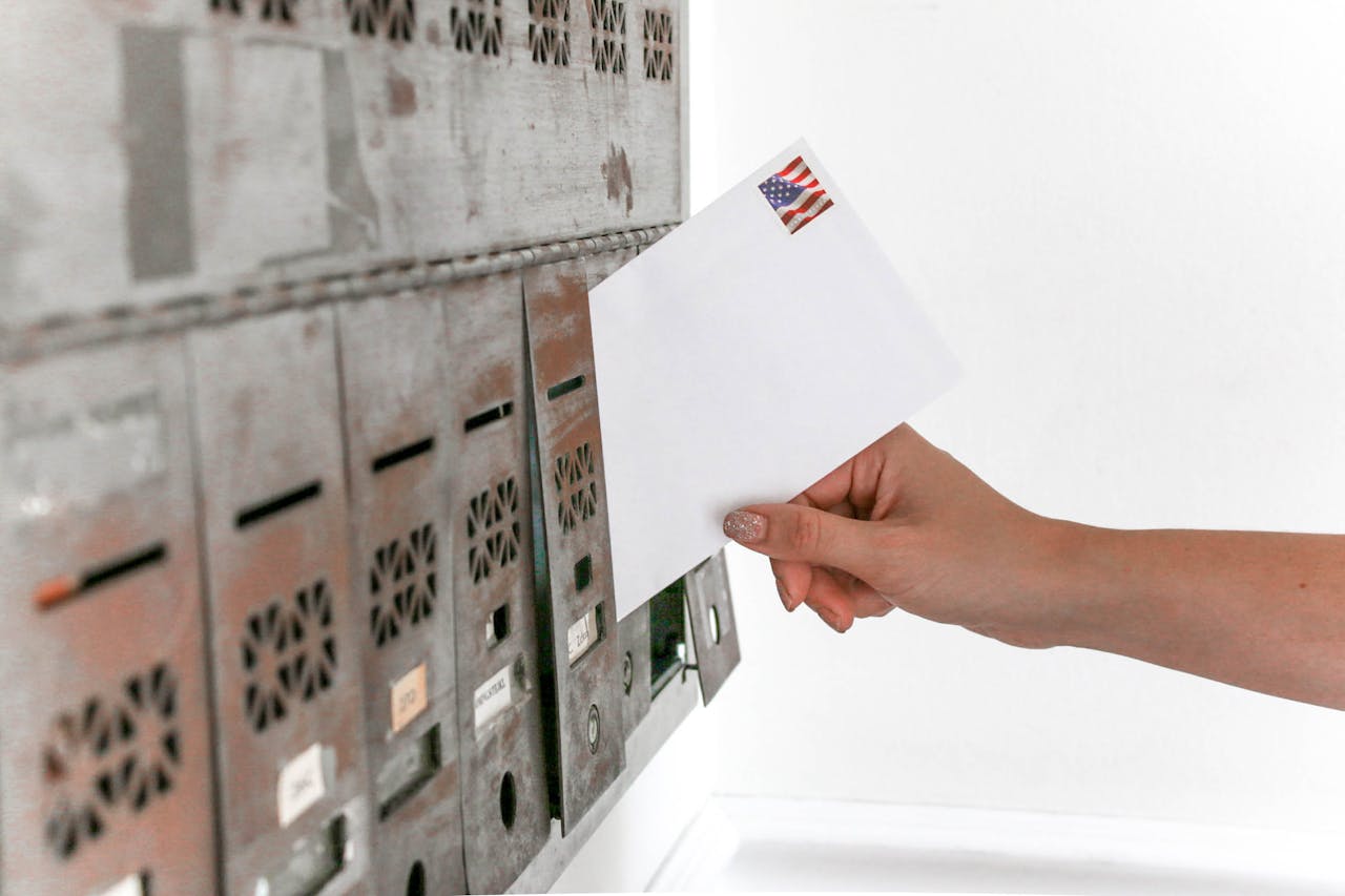 Person holding an envelope in their hand in front of multiple mailboxes. Image by Pexels