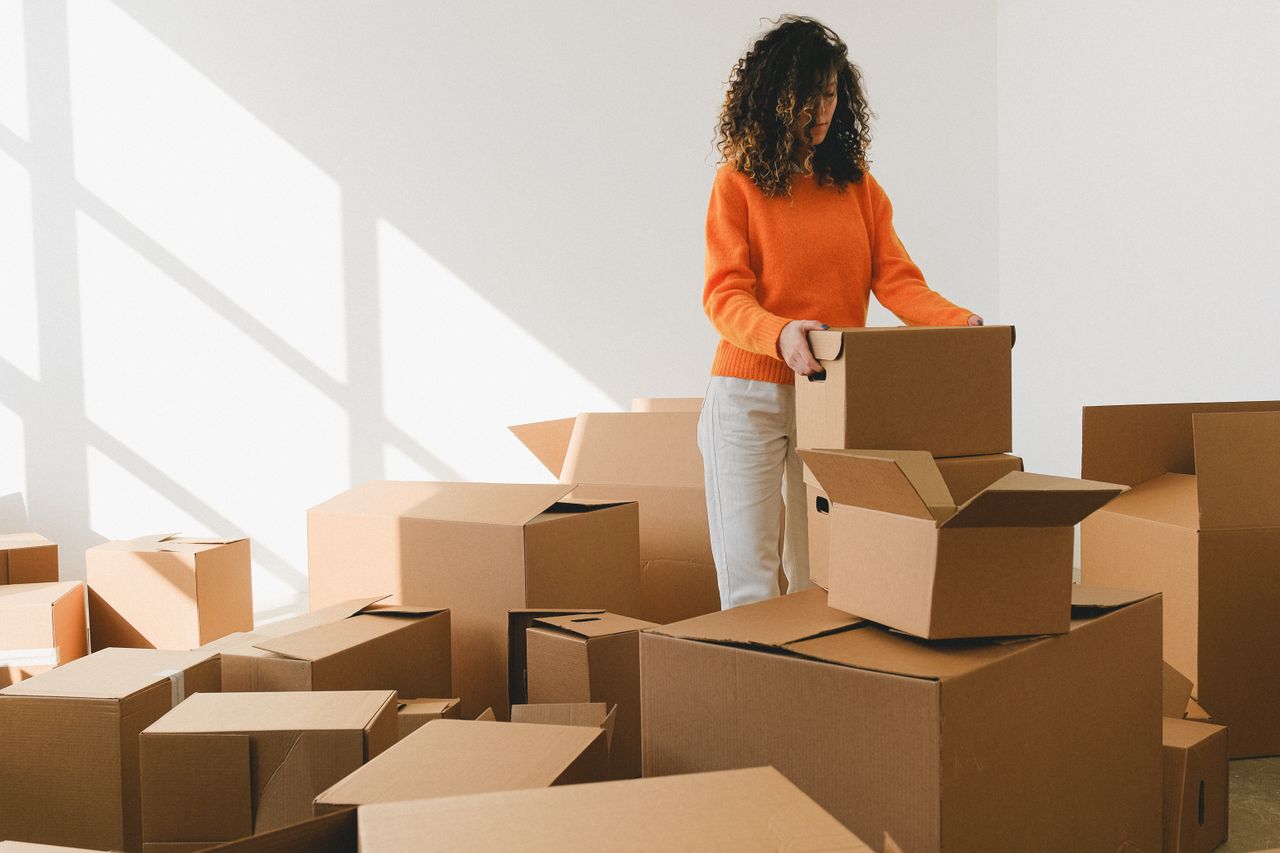 A woman organizing cardboard boxes in a bright room, preparing for relocation