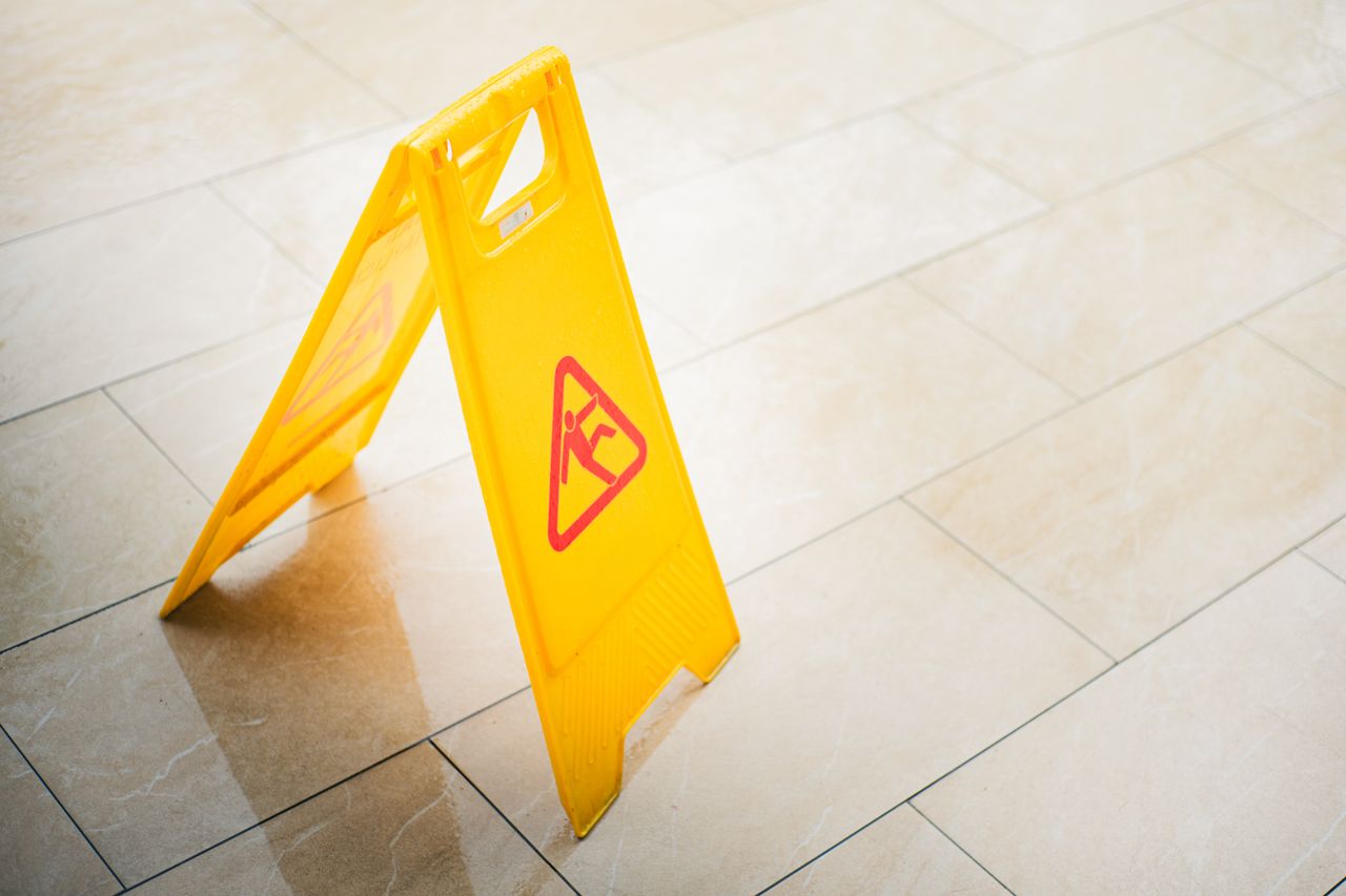 A bright yellow caution sign on a tiled floor indicates a wet surface, alerting passersby to potential hazards. Image by Pexels