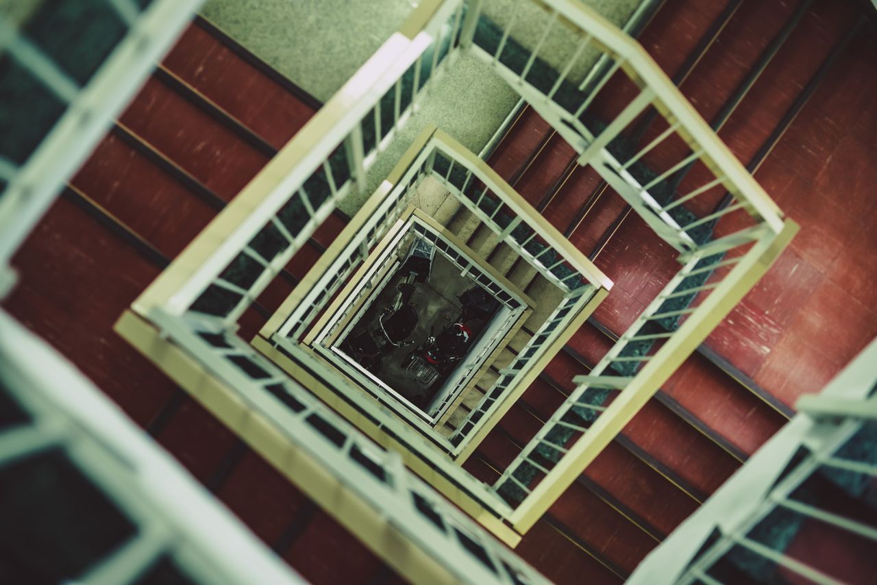 A high angle view of a spiral staircase with red steps and contrasting handrails creates a dramatic visual effect. Image by Pexels